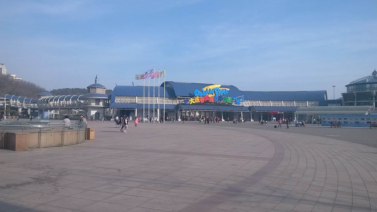La place d’entrée et les halls d’exposition du parc océanique de Laohutan sous un vaste ciel bleu.