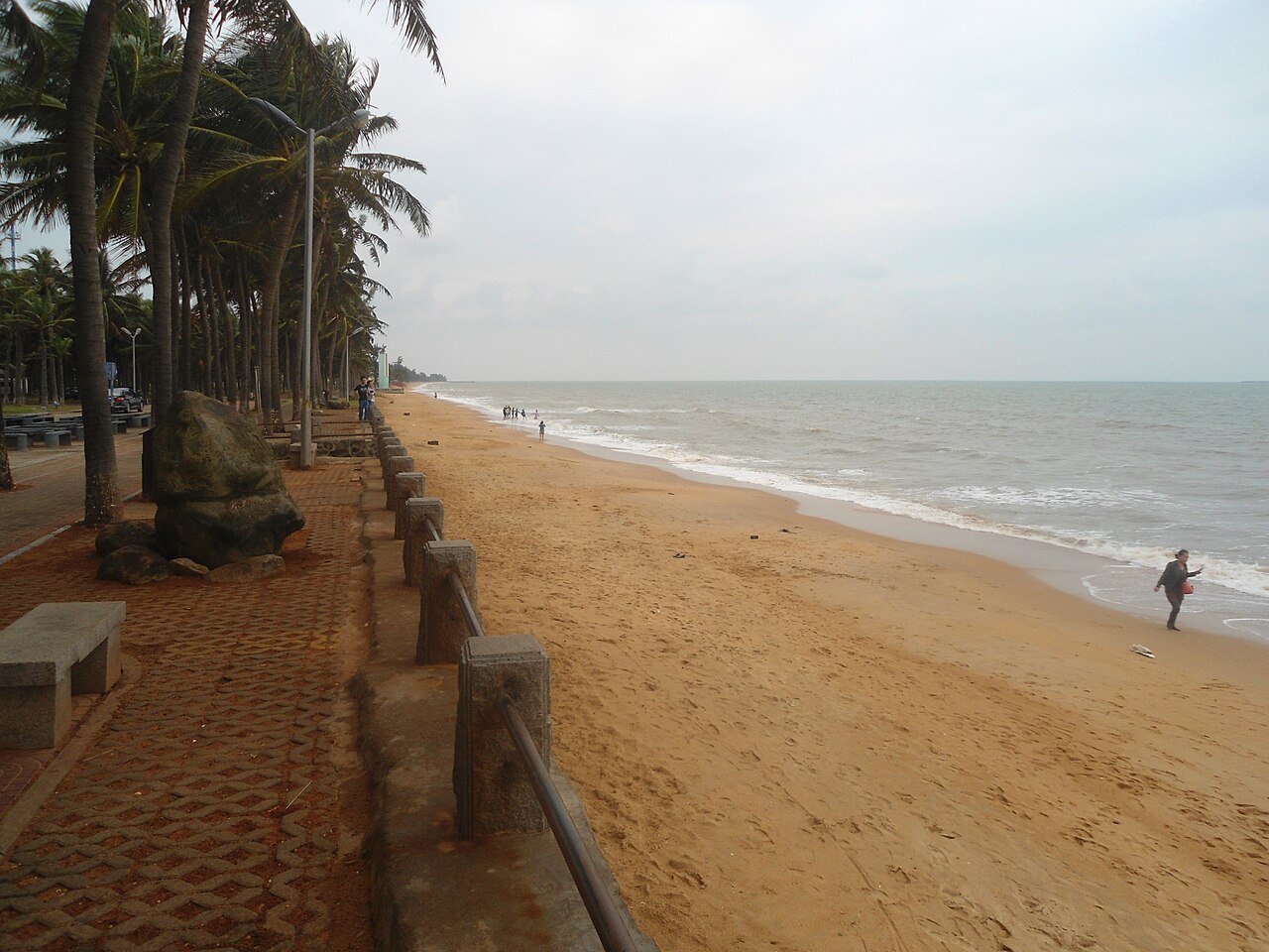 ต้นปาล์มเรียงรายบนผืนทรายสีทองของหาดฮอลิเดย์บีช นักเดินคนหนึ่งเดินอยู่ริมทะเลอันเงียบสงบ