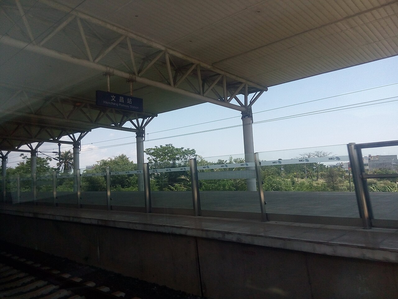 El andén de la estación de tren de Wenchang, con el nombre de la estación en chino e inglés en un cartel azul bajo la marquesina.