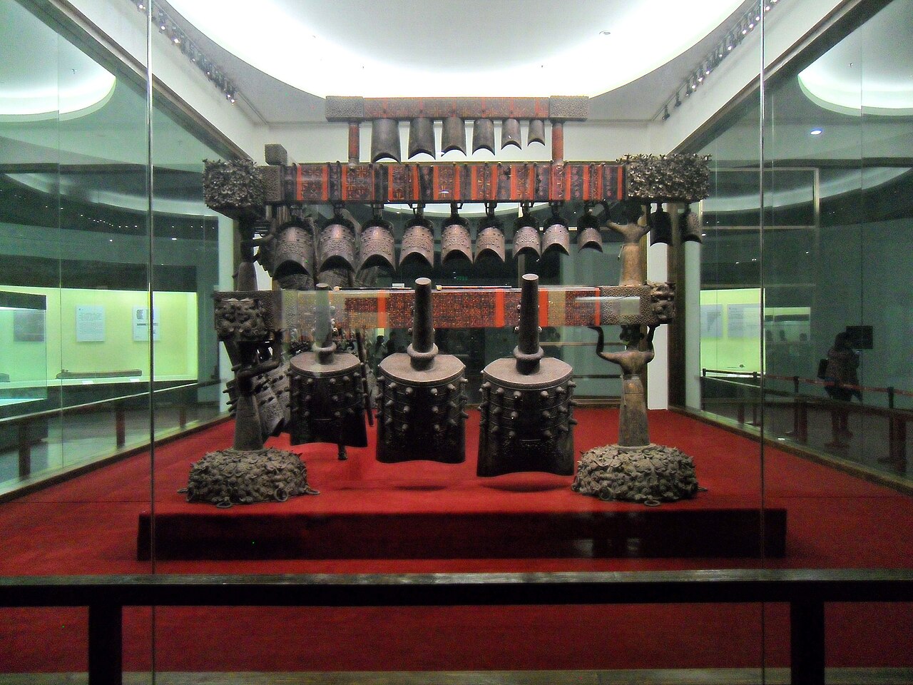 Hileras de antiguas campanas de bronce colgadas en un armazón de madera escalonado en una galería oscura del museo