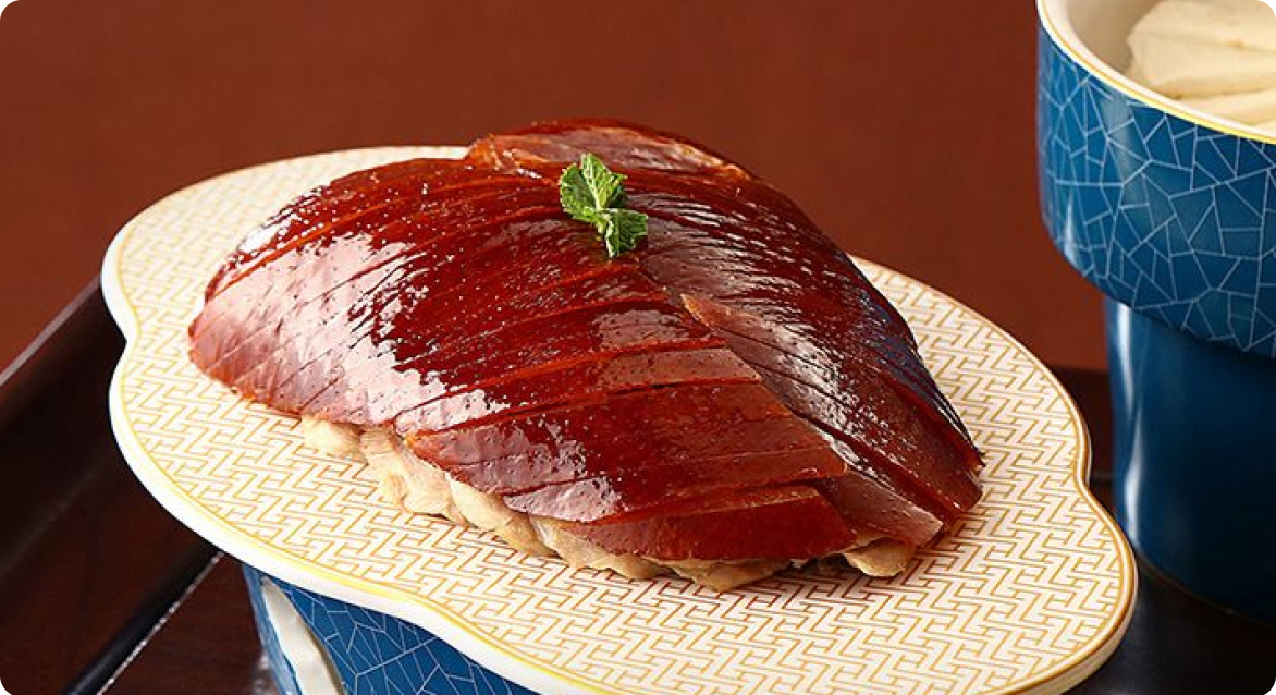 Sliced Peking duck on a patterned plate, with a bowl of pancakes beside it