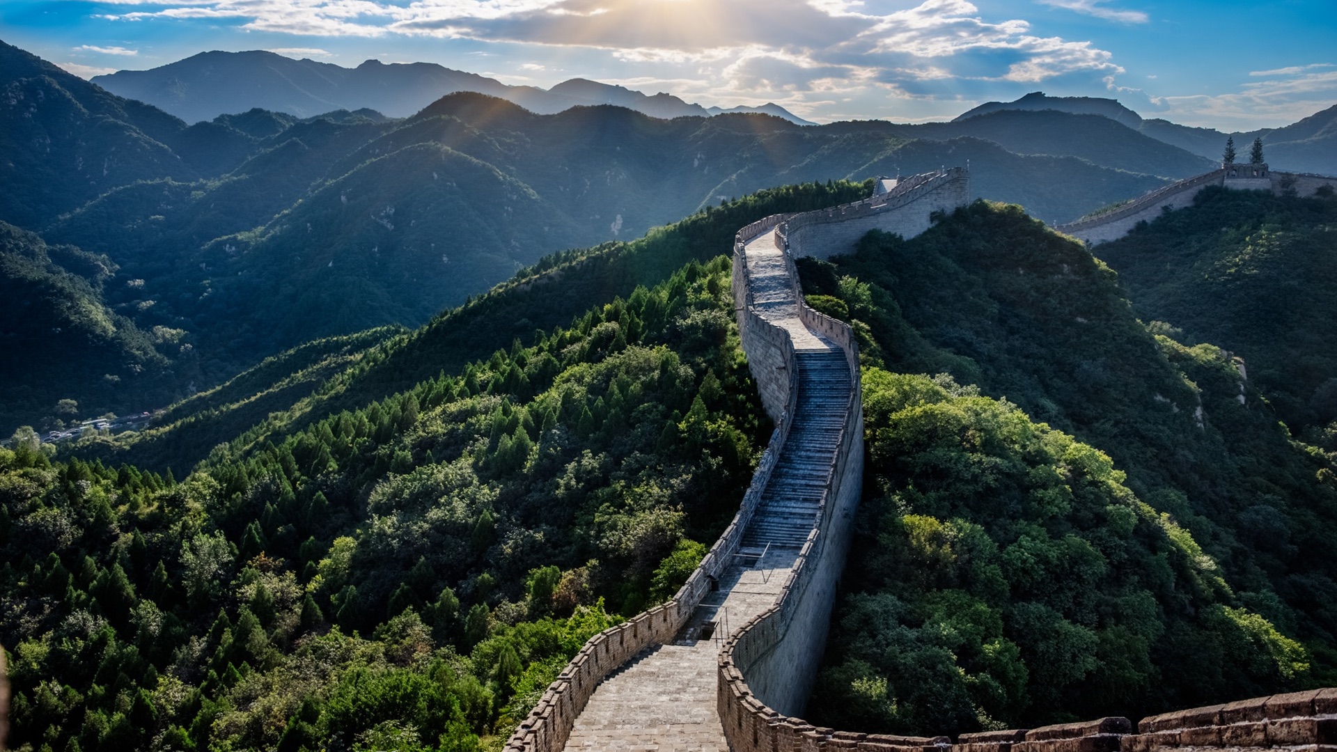The Great Wall climbing a forested ridge in afternoon light, its walkway empty of visitors