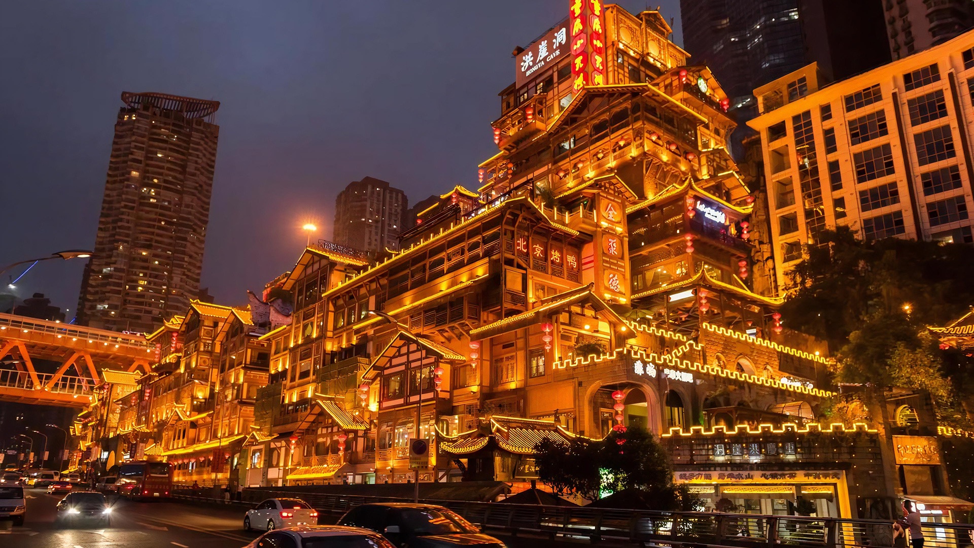 The Hongyadong stilt houses lit gold at night above the road in Chongqing