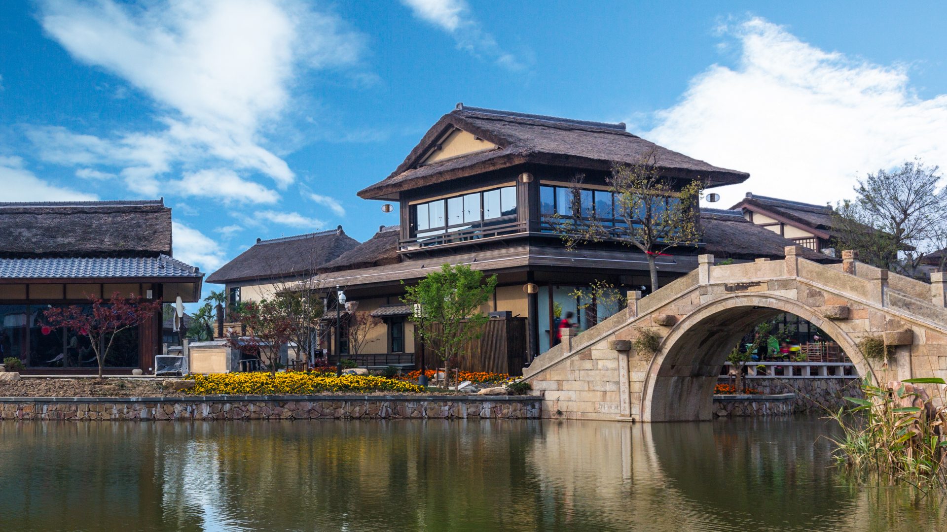 A stone arch bridge over still water at Lizhuang Ancient Town, with tiled timber halls behind
