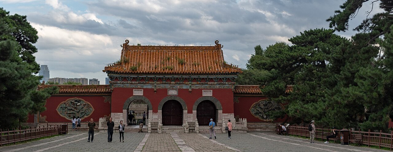 The red ceremonial gate of Zhao Mausoleum framed by ancient pine trees in Beiling Park